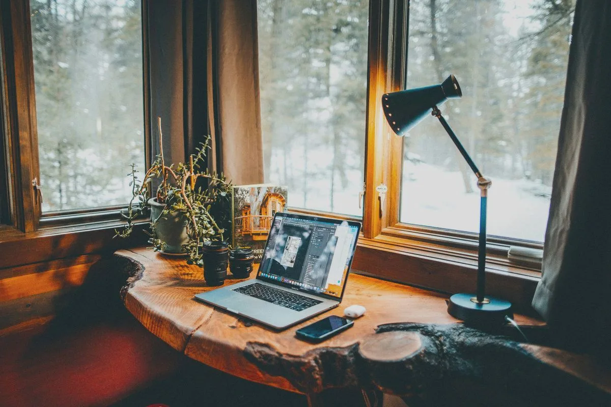 A laptop on a wooden worktop by a window looking out on a snowy forest