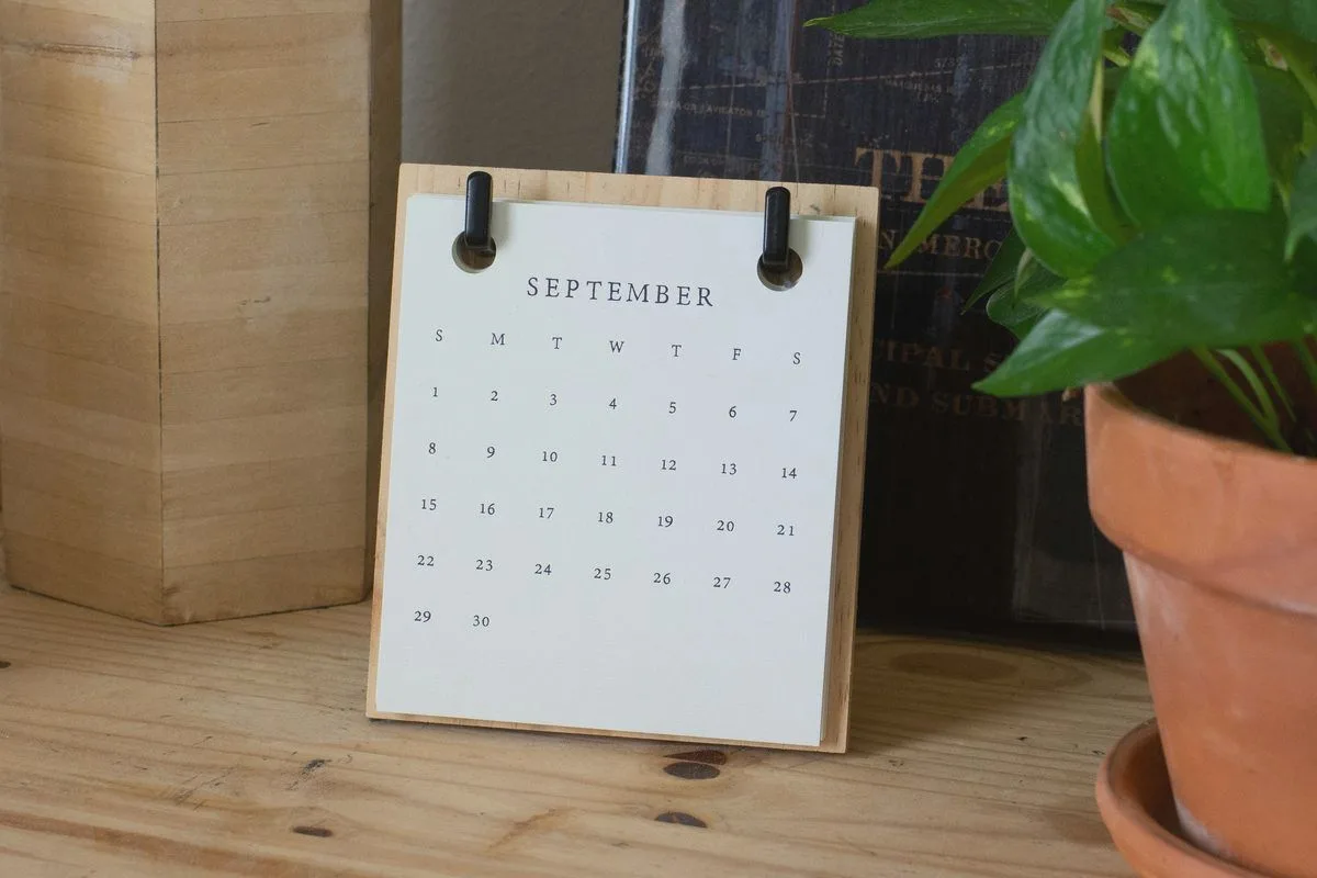 A desk calendar leaning against the wall next to a potted plant